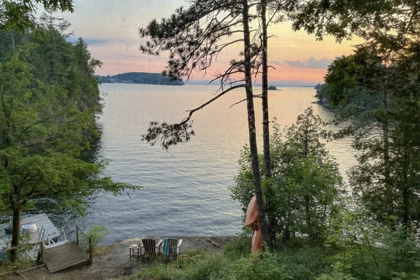 Lakeside beach with Adirondack chairs, dock, and forested shoreline at sunset