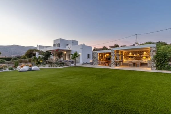 Modern white villa with stone pavilion, manicured lawn, and mountain views at dusk